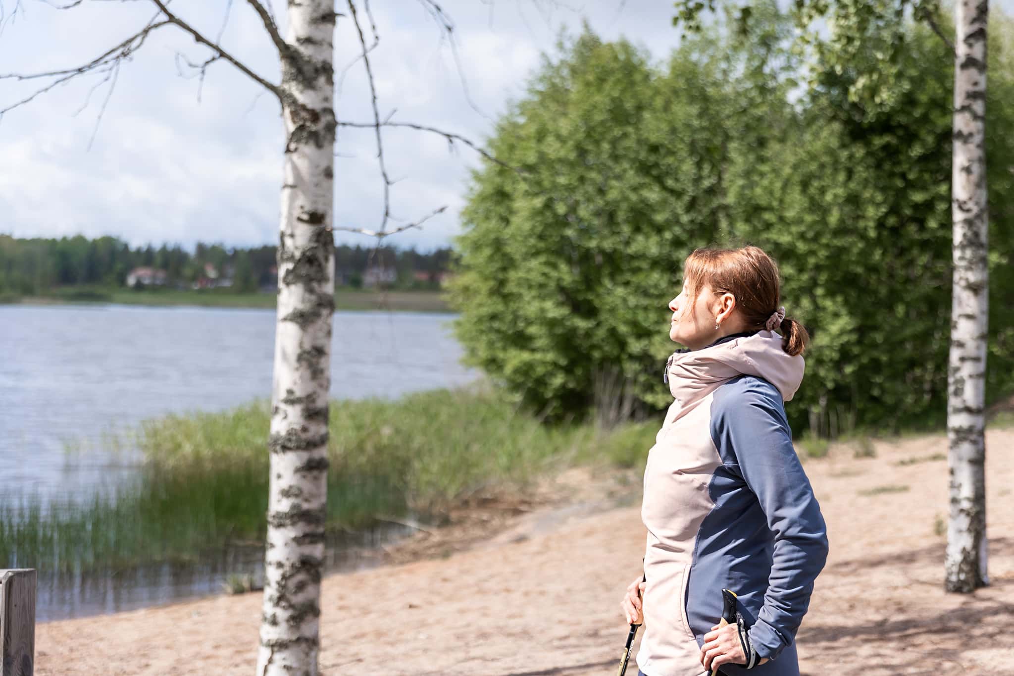 Nainen hengittelee Kunnonlähteen rannassa koivujen keskellä